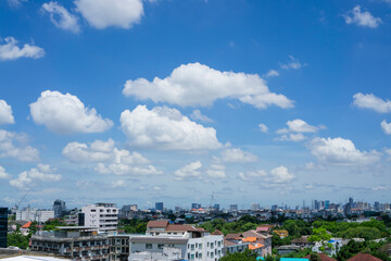 White fluffy clouds on vivid blue sky above a city, view from rooftop 