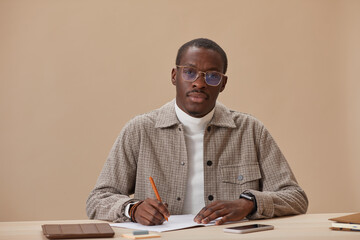 Fototapeta premium Portrait of African young man in eyeglasses sitting at the table with books and studying