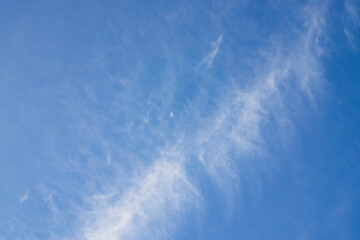 Upward view, white fluffy clouds on blue sky and small crescent moon 