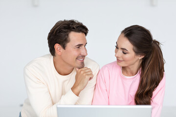 Young happy couple with laptop looks at each other.