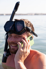 young man in a mask and a snorkel at sea speaks on the phone and laughs. tell your friends about...