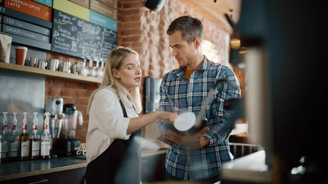Two Diverse Entrepreneurs Have a Team Meeting in Their Stylish Coffee Shop. Barista and Cafe Owner Discuss Work Schedule and Menu on Tablet Computer. Young Female and Male Restaurant Employees.
