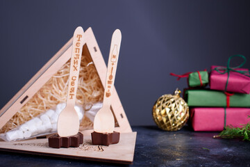 A wooden box gift with a marshmallows for coffee and spoons with chocolates in the form of a star Christmas tree. New Year's content.