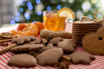 christmas gingerbread cookies and cinnamon on a red checkered tablecloth next to citrus tea and ginger on the background of a christmas tree