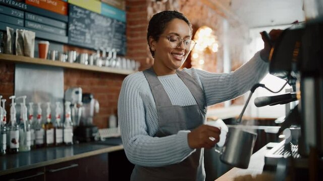 Beautiful Latin American Female Barista with Short Hair and Glasses is Making a Cup of Tasty Cappuccino in Coffee Shop Bar. Portrait of Happy Employee Behind Cozy Loft-Style Cafe Counter.