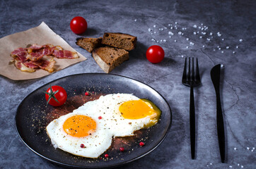 Breakfast with fried eggs on a grey concrete background with bacon, bread and tomatoes