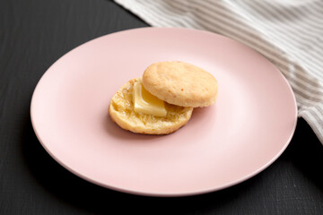 Homemade Flaky Buttermilk Biscuit on a pink plate on a black surface, low angle view.