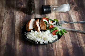 Ready chicken breast with rice and salad. All food on a black plate