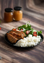 Ready chicken breast with rice and salad. All food on a black plate
