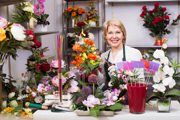 Friendly smiling mature female florist with clippers making flowers ready for sale.
