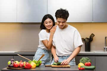 Loving Asian Wife Embracing Husband While Cooking Together In Kitchen