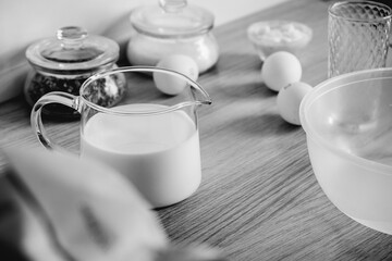 eggs, a decanter with milk on the table and a whisk, the main background of baking. Home cooking. Black and white