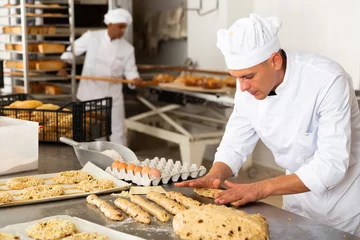 Gordijnen Portrait of man baker working with dough and forming baguettes © JackF