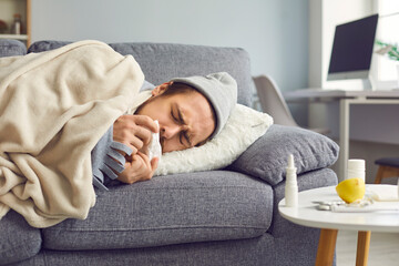 Close up of a sick man with a runny nose with a napkin in his hands lying on the couch.