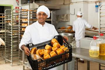 Baker with box with baguettes in bakery kitchen