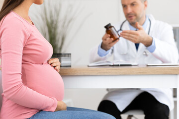 Mature experienced doctor showing pills to pregnant lady