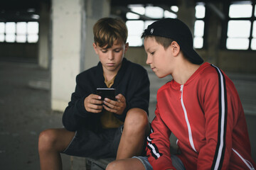 Group of teenagers boys indoors in abandoned building, using smartphone.