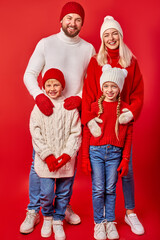 portrait of positive smiling family with children isolated on red wall, beautiful parents and children in winter clothes in a good modd, Xmas and New Year 2021 concept