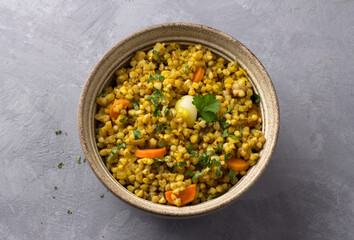Healthy homemade food bowl with green buckwheat, vegetables (onions, carrots, garlic), greens and curry with glass of water on gray textured background