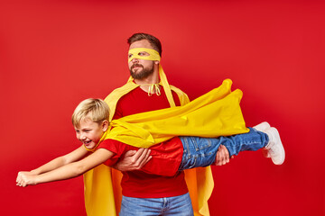 powerful man holding little kid boy in hands, like superhero, want to fly. isolated on red...