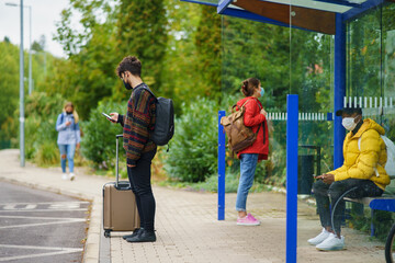 Young people with smartphone on bus stop outdoors in town. Coronavirus concept.