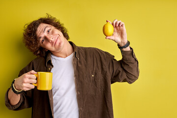 It's cold and emidemic outside happy attractive guy enjoying fresh aromatic tea with lemon, isolated on yellow background, smile