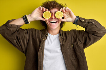 handsome curly teen boy laughing and making fun with lemon isolated over green background, studio portrait