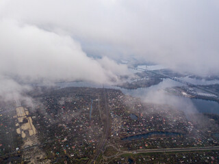 High aerial flight in the clouds over Kiev. An autumn cloudy morning, the Dnieper River is visible on the horizon.