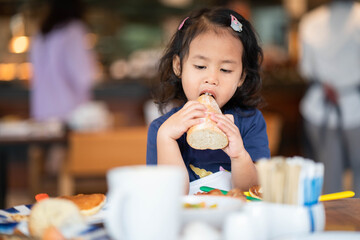 Cute little girl sitting at table eating baguette. 