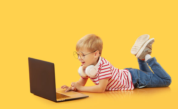 Litttle child boy using laptop on yellow background. Education, online study, home studying, distance learning. Primary school student during quarantine