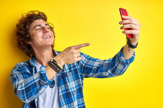 happy caucasian man take photo of himself on smartphone, selfie on mobile phone, isolayed yellow background