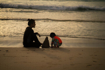 Silhouette mother and daughter building sand castle at the beach.