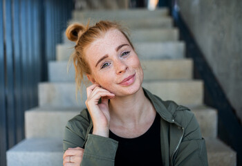 Fototapeta premium Front view portrait of young woman with red hair outdoors in town, looking at camera.