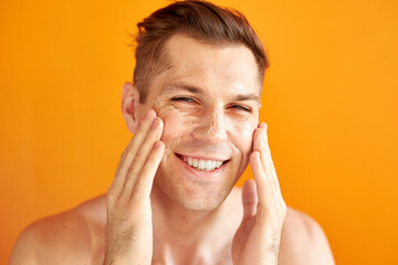 european guy moisturizes face skin for getting healthy skin, uses beauty cream, studio shoot isolated over orange background