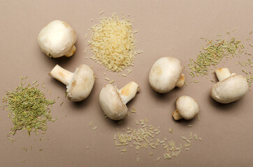 Top view of white mushrooms, heaps of rice and dried rosemary on the bright brown background