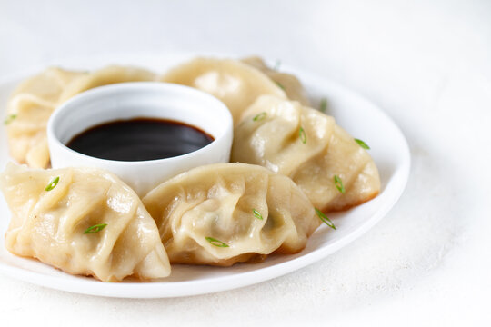 Japanese gedza dumplings on a white plate with soy sauce and green onions