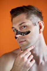 handsome caucasian man with skin care patch on nose, isolated on orange background, shirtless male is using cleansing strip for nose