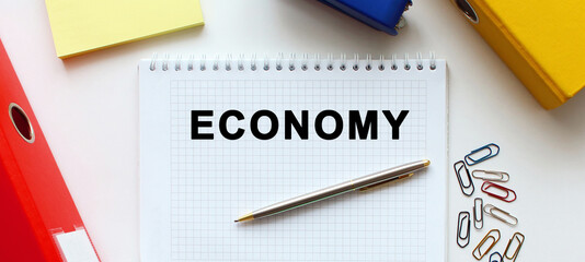 Notepad with text ECONOMY on a white background, near document folder and office supplies.