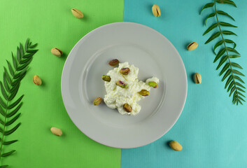 Pistachios on fresh cheese, served on a white porcelain plate. Two-color background 