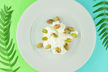 In this case pistachios on fresh cheese, served on a white porcelain plate. Two-color background with small natural leaves.