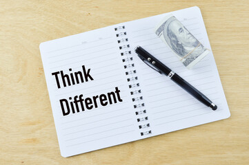 Top view of pen, banknote and notebook written with text THINK DIFFERENT over wooden background. Business and education concept.