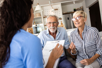 Female nurse talking to seniors patients while being in a home visit, senior couple signs an...