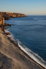 Wild pebble beach near Playa San Juan towards the banana plantations on the top of the rough cliffs, familiar volcanic landscape of the eastern coast of the island of Tenerife, Canary Islands, Spain