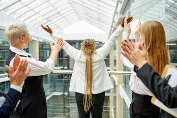 rear view on happy afro woman with raised hands, colleagues celebrating the win. african female get congratulations