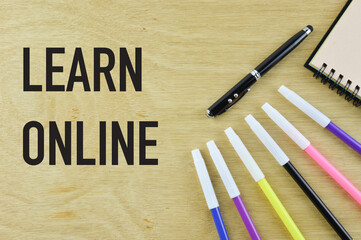 Selective focus of notebook, color and pen on a wooden background written with text LEARN ONLINE.
