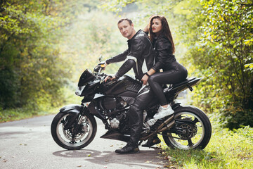Fototapeta na wymiar Loving couple, guy and girl bikers, in black leather clothes. near a sports motorcycle on a forest road
