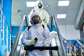 disinfection service on escalator in the building, team of sanitation workers in suit using...