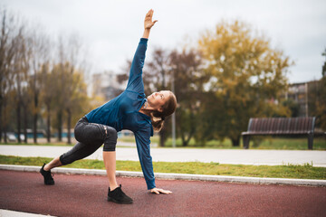 Beautiful adult woman is exercising outdoor on cloudy day in autumn.