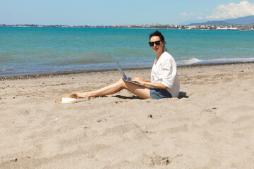Young woman using laptop computer on a beach. Vacation lifestyle communication. Freelance work concept