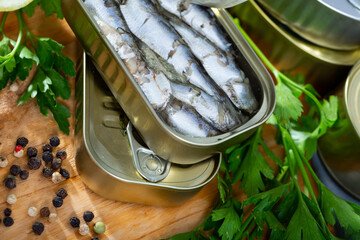 Appetizing pilchards in marinade of oil in open tin can on wooden table with greens and lemon
